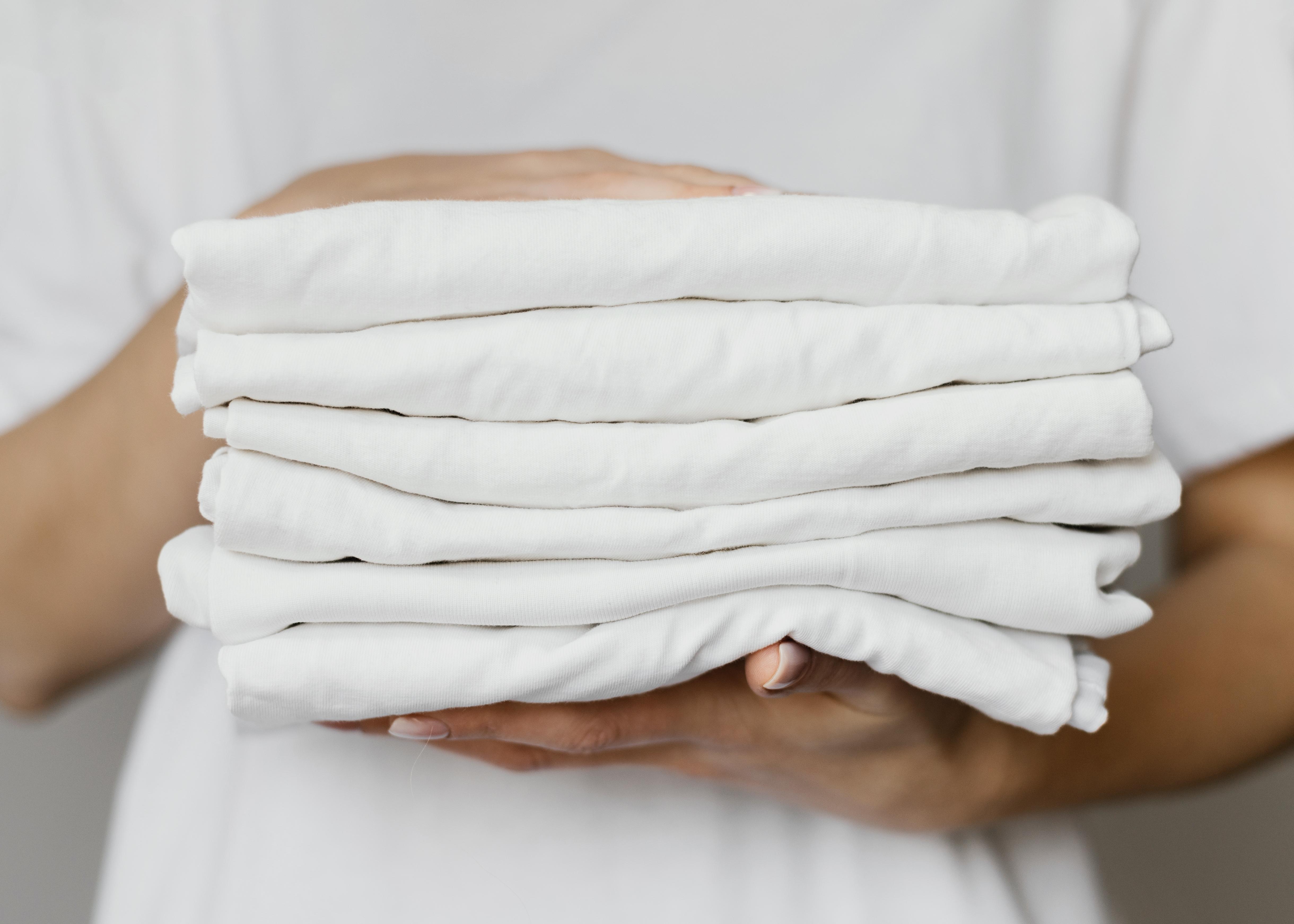 person holding stack of white clothes