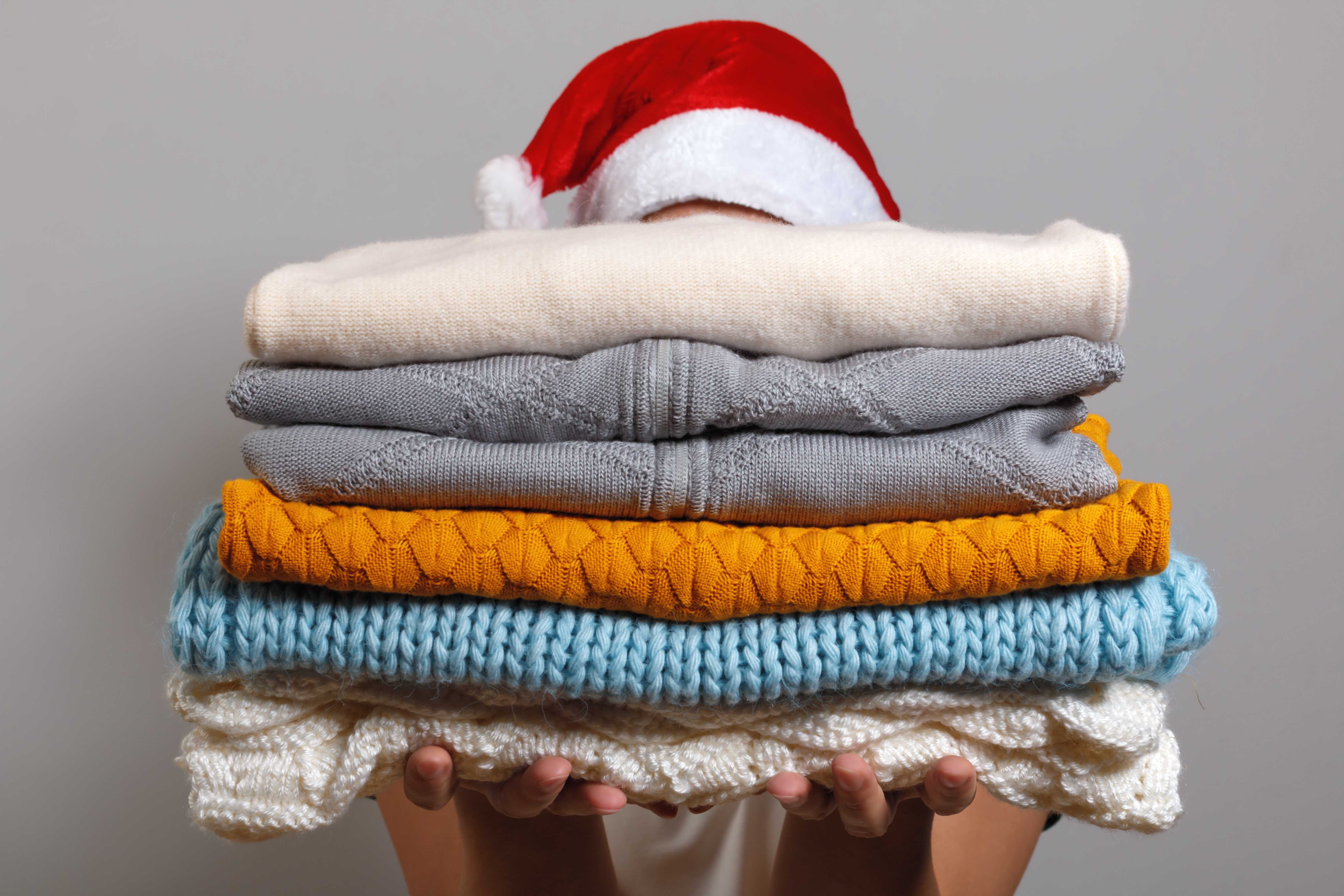 The image shows a woman holding folded winter clothes in her hands. 
